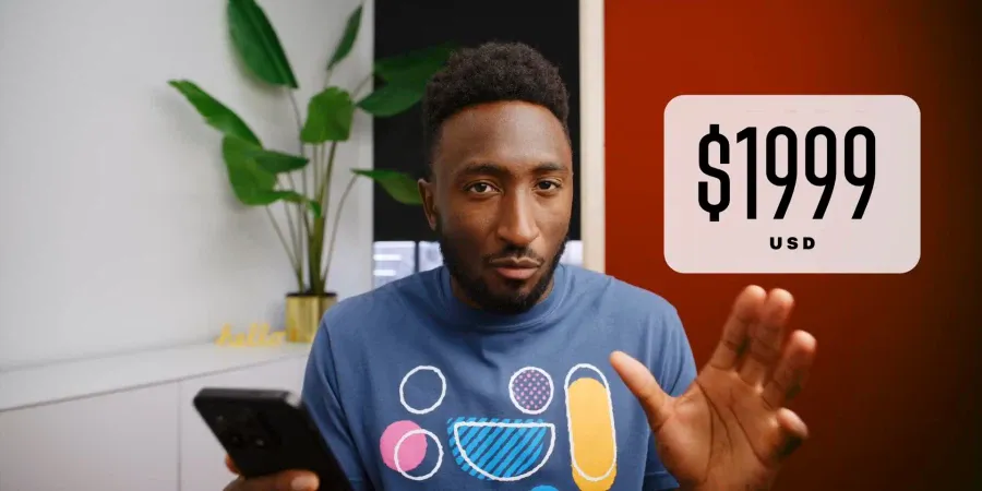 A YouTuber holding a smartphone gesturing next to a graphic showing $1,999 (USD)