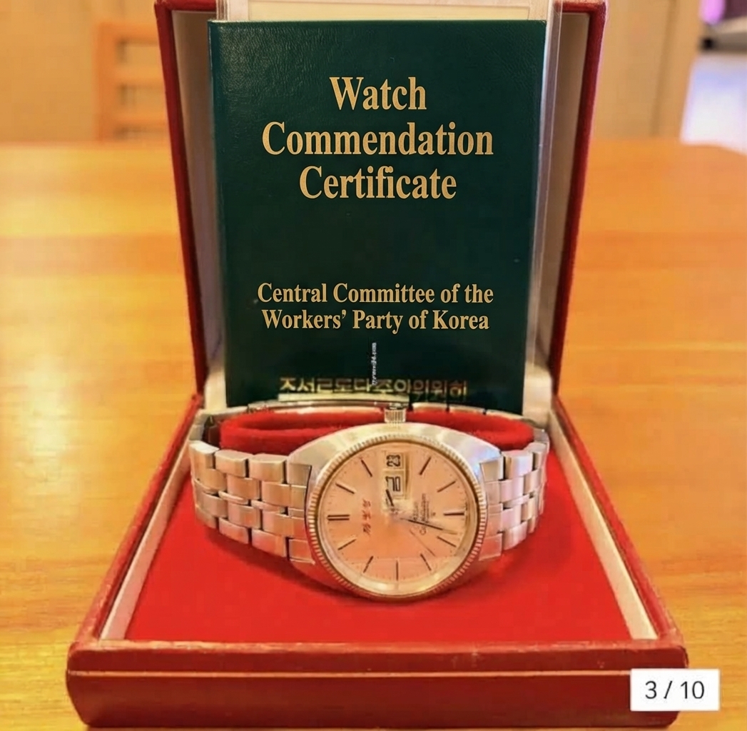 An Omega watch featuring a Hangul day-of-the-week display resting inside a red case alongside a green watch commendation certificate booklet