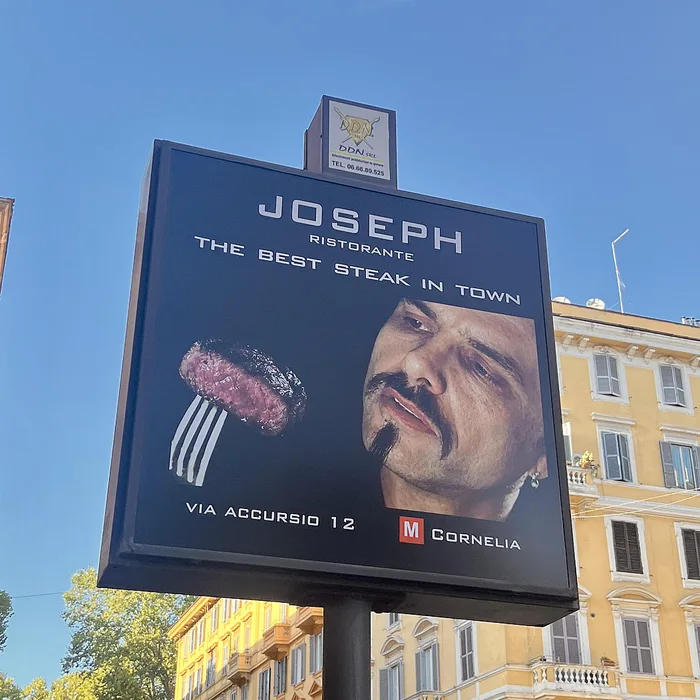 A street sign advertisement for Joseph Ristorante reading 'The Best Steak in Town', featuring Cypher from The Matrix looking at a steak on a fork.
