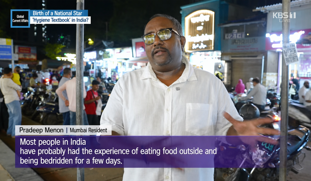 A screen capture of a KBS1 broadcast. During an interview, Mumbai resident Pradeep Menon says, "Most Indians have had the experience of being bedridden for a few days after eating out."