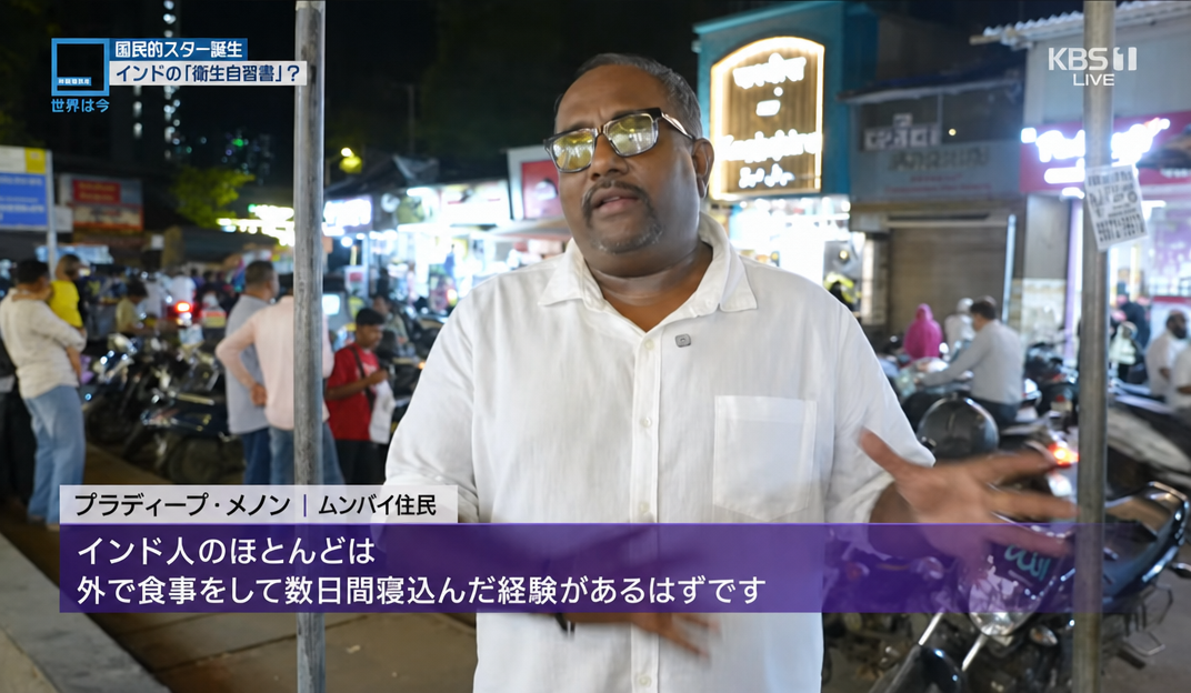 KBS1の放送画面のキャプチャ。インタビューに応じるインド・ムンバイの住民プラディープ・メノンが、「インド人のほとんどは、外で食事をして数日間寝込んだ経験があるはずです」と語っている。