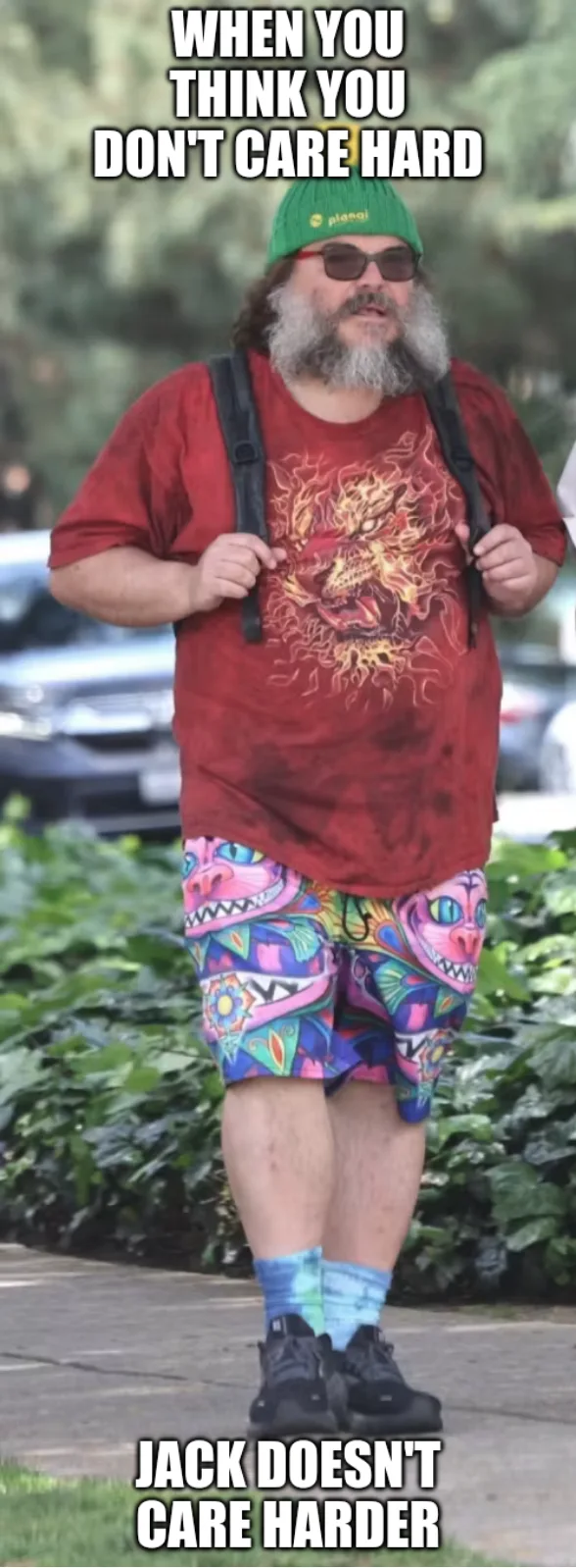 Jack Black walking outdoors wearing a green beanie, graphic tee, and bright colorful shorts.