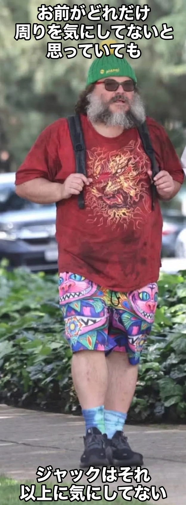 緑のビーニー、グラフィックTシャツ、カラフルで派手なショートパンツを身につけて屋外を歩くジャック・ブラック。